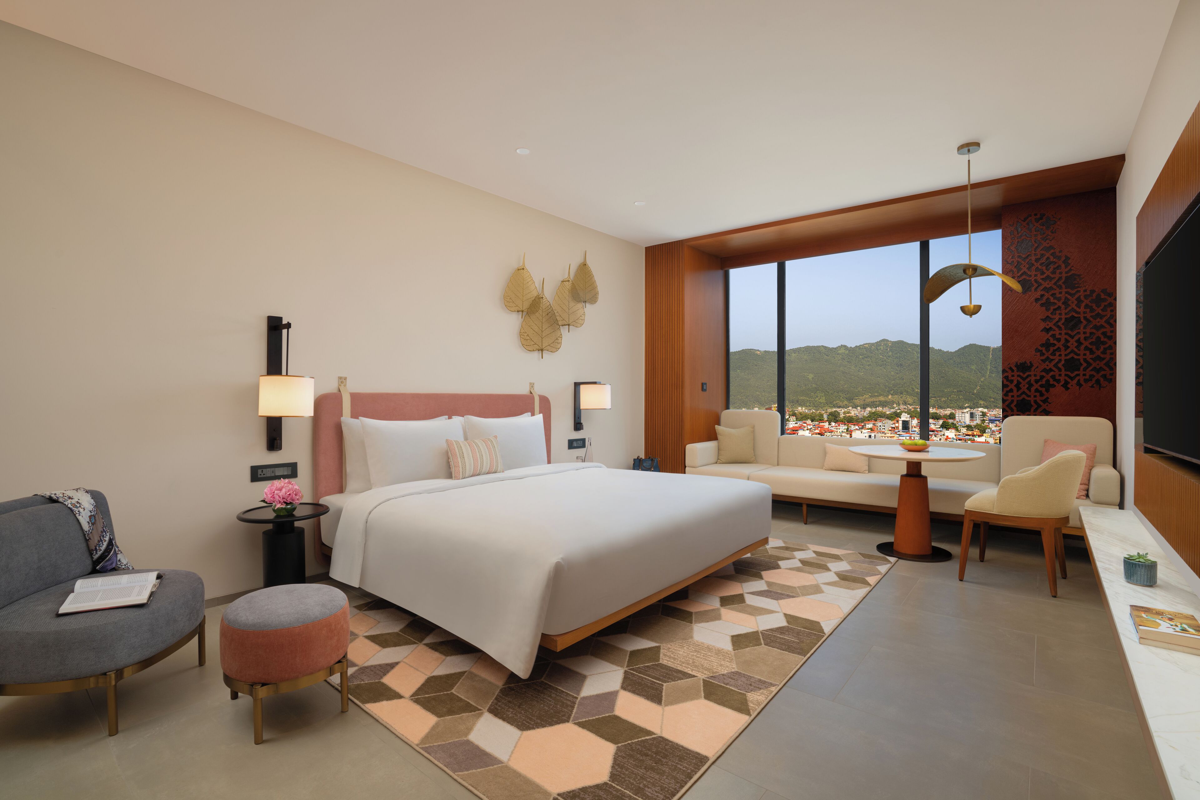 Habitación de hotel con cama, sofá, sillón, mesita y vista a un paisaje urbano.