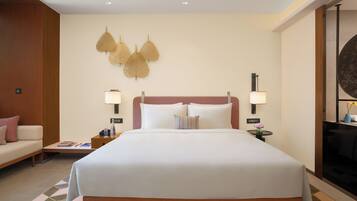 Quarto de hotel com uma cama grande, duas mesas de cabeceira, um criado-mudo, um sofá e um objeto decorativo na parede.