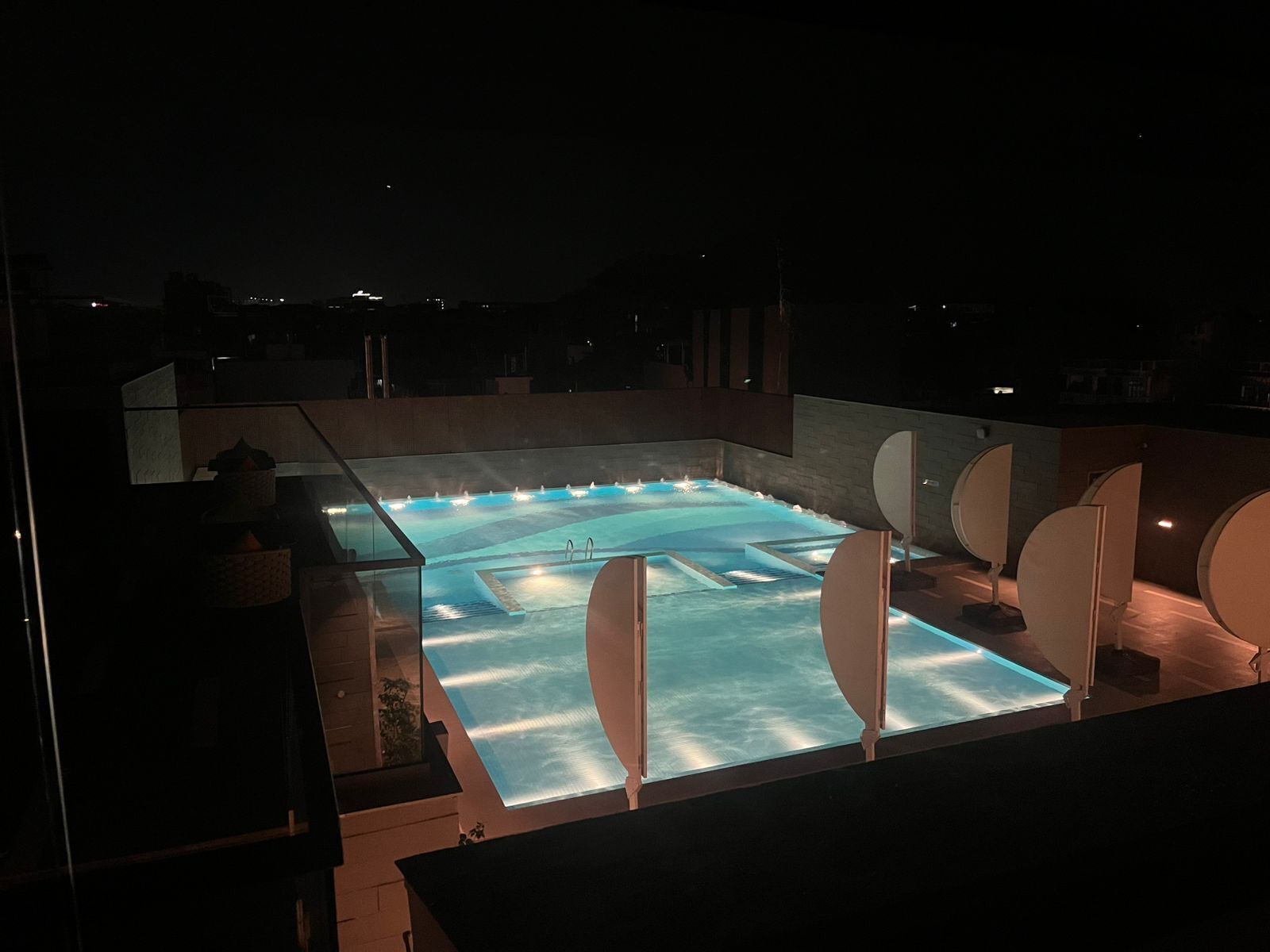 Una piscina en la azotea con cerramiento de cristal, rodeada de elementos arquitectónicos modernos y vista al cielo nocturno.