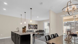 A modern kitchen with a central island, dining area with a glass table, and a living space with a sofa and coffee table. - Last Minute Disney Getaway! Private Pool & Themed Bedrooms. Book Now! #150581 (Orlando)