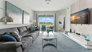 En moderne stue med en grå sofa, et sofabord og et fjernsyn monteret på væggen.