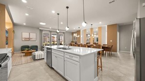 Een moderne keuken met een centraal eiland, hanglampen en een eethoek met houten stoelen en een tafel.