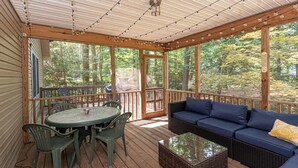 Une terrasse couverte avec une table et des chaises, un canapé et une grande fenêtre donnant sur la forêt.