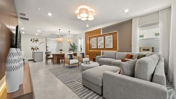 Una sala de estar moderna con un sofá gris, un comedor con mesa de madera, y una cocina al fondo.
