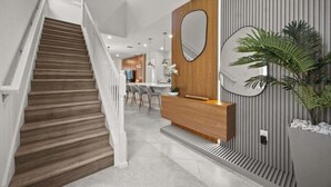 Un interior moderno con una escalera de madera, una zona de cocina y un espacio de estar con un espejo grande y plantas.