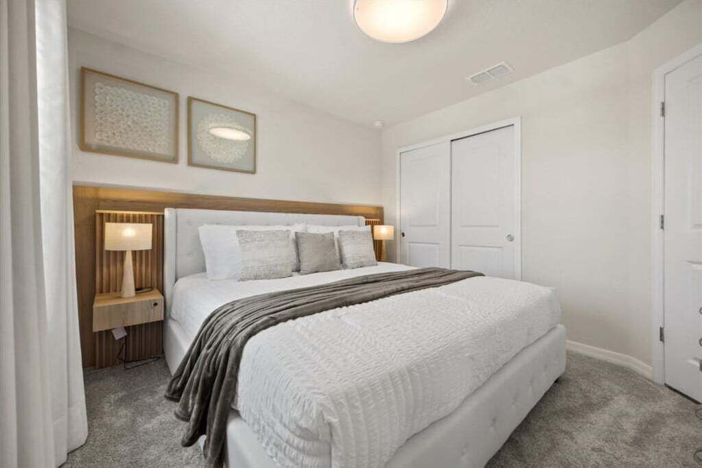 A bedroom with a large bed, two bedside tables with lamps, a wooden headboard, and a door.