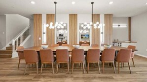 Een moderne eethoek met een lange houten tafel, zes stoelen en hanglampen.
