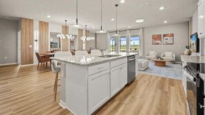 Een moderne keuken met een groot eiland, witte kastjes en hanglampen.