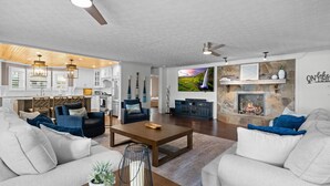 Una sala de estar moderna con chimenea, un comedor con candelabro y una cocina con armarios blancos.