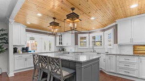 Una cocina con armarios blancos, una isla central con taburetes de bar, iluminación colgante y techo de madera.