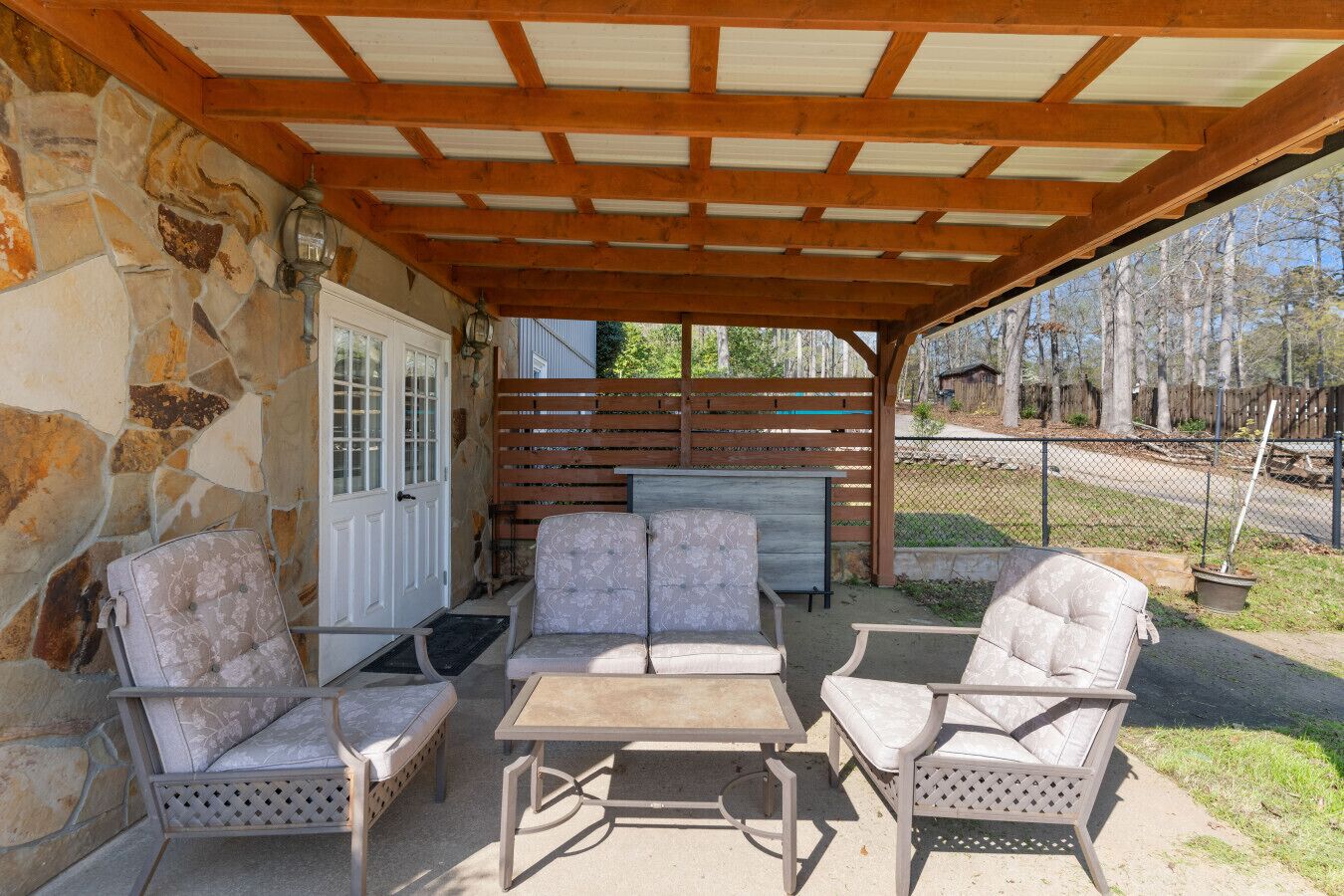 An outdoor patio with stone walls, a covered seating area with chairs and a table, and a stone door.