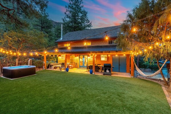 A cozy log cabin with a hot tub, outdoor seating, and string lights. - Stargazer’s Sanctuary • Observatory Dome Retreat: Sauna & Hot Tub (Sedona)