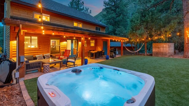 En træhytte med jacuzzi, udendørs møbler og lyskæder.