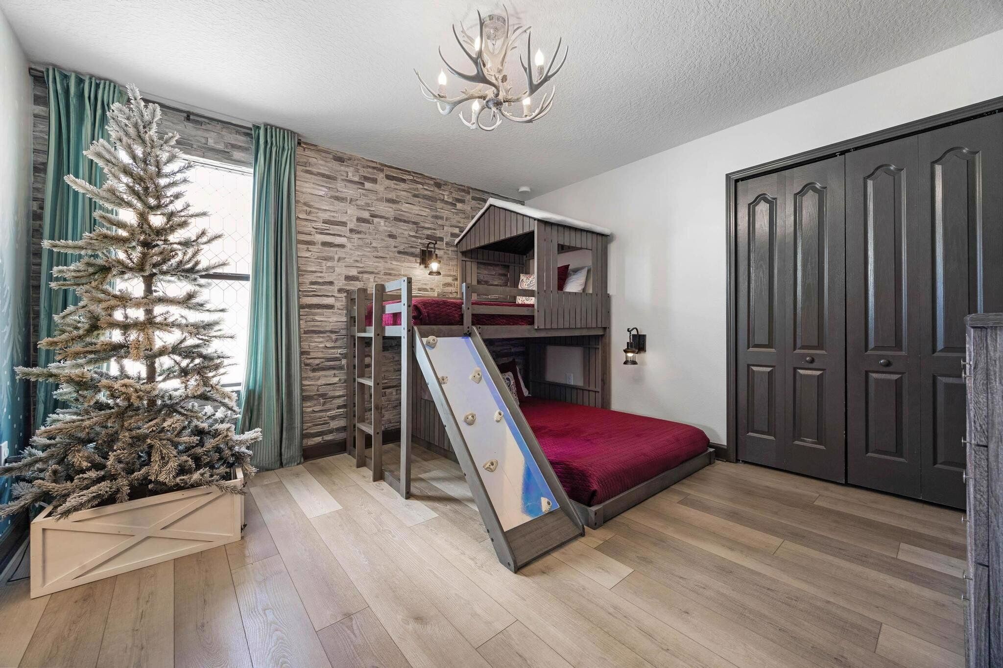 A bedroom with a bunk bed, a sliding ladder, a Christmas tree, and a wardrobe.