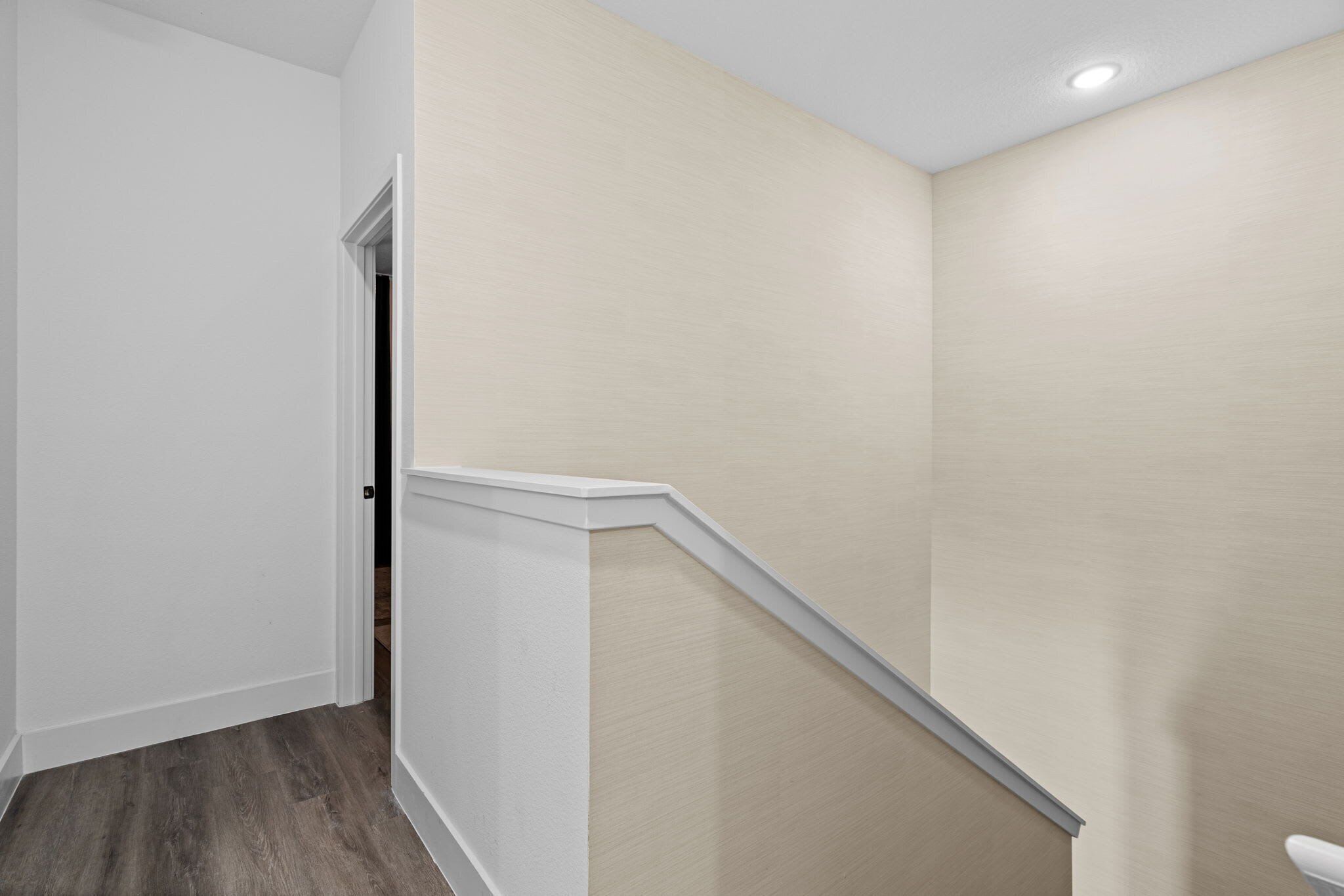 Un pasillo con piso de madera, paredes blancas y una pared de acento color beige.