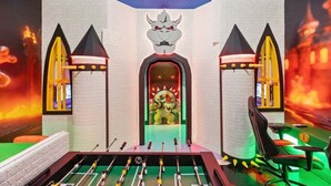 Una habitación con mesa de futbolín, un ventanal con vista a un paisaje rojizo, y un arco decorativo en la pared con una estatua de león.