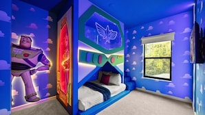 Una habitación con literas, una ventana con vistas a la vegetación y una pared con un póster de Buzz Lightyear.