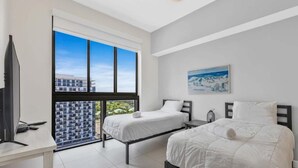 A modern hotel room with two beds, a desk, and a large window offering a city view. - DTW Doral 2 BD Condo and Skyline Views (Miami)