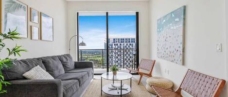 Ett modernt vardagsrum med en grå soffa, ett runt soffbord och två stolar. Ett stort fönster ger utsikt över stadsbilden.