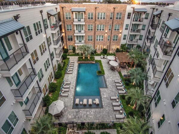 A multi-story residential building with a central courtyard featuring a swimming pool, lounge chairs, and outdoor seating.
