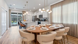Cozinha moderna com armários brancos, uma ilha central e uma área de refeições com mesa e cadeiras de madeira.