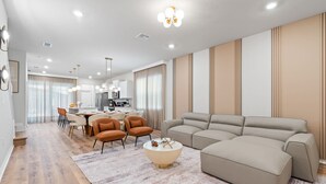 Uma sala de estar moderna com um sofá, mesa de centro e cadeiras. Ao fundo, há uma área de jantar com uma mesa e cadeiras.