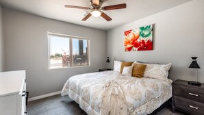 Une chambre à coucher avec un lit, un ventilateur de plafond, une fenêtre, une table de chevet et un tableau.