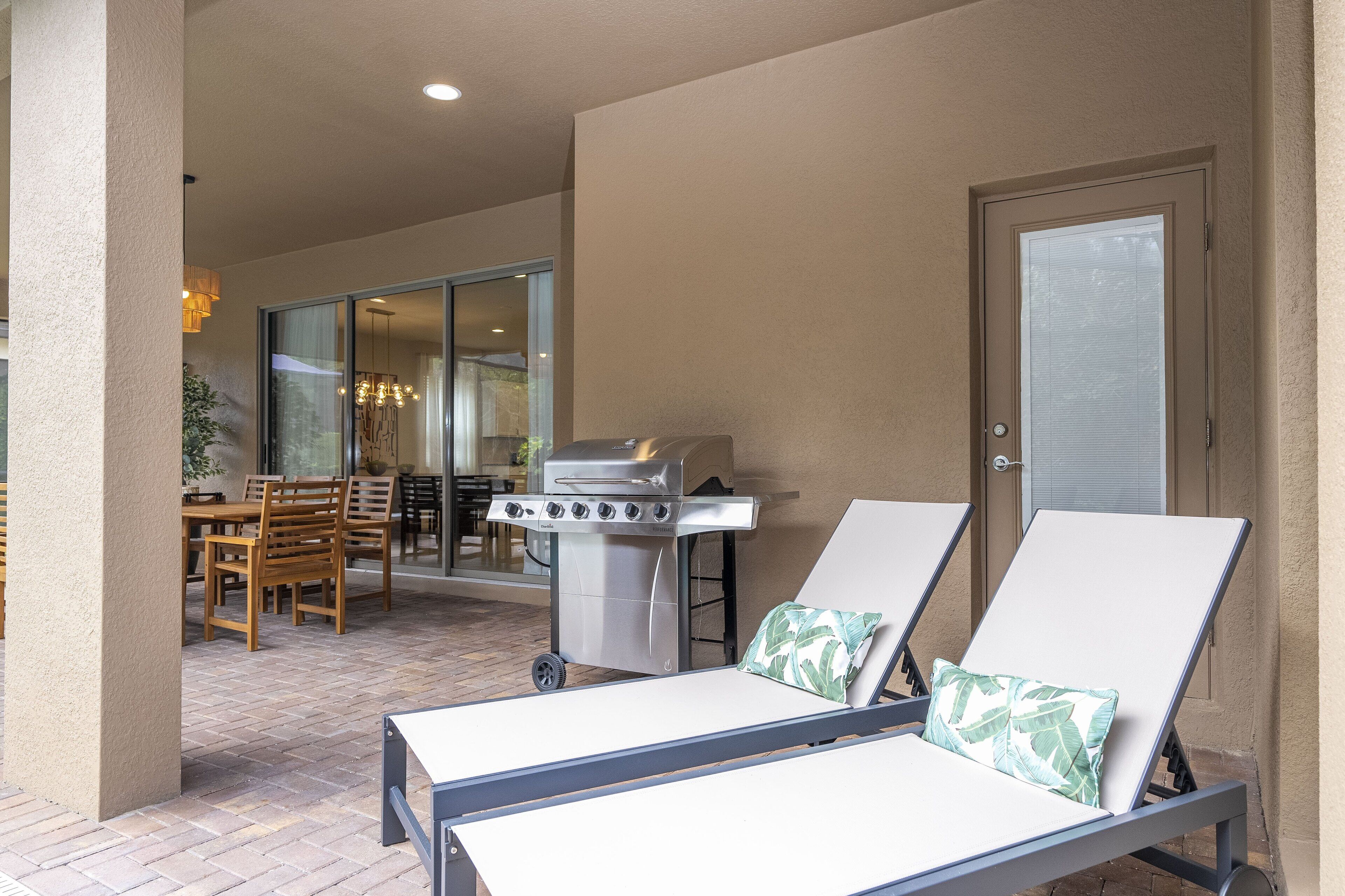 A patio with two lounge chairs, a grill, and a dining area with chairs and a table.
