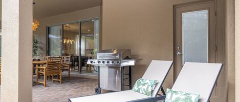 A patio with two lounge chairs, a grill, and a dining area with chairs and a table.