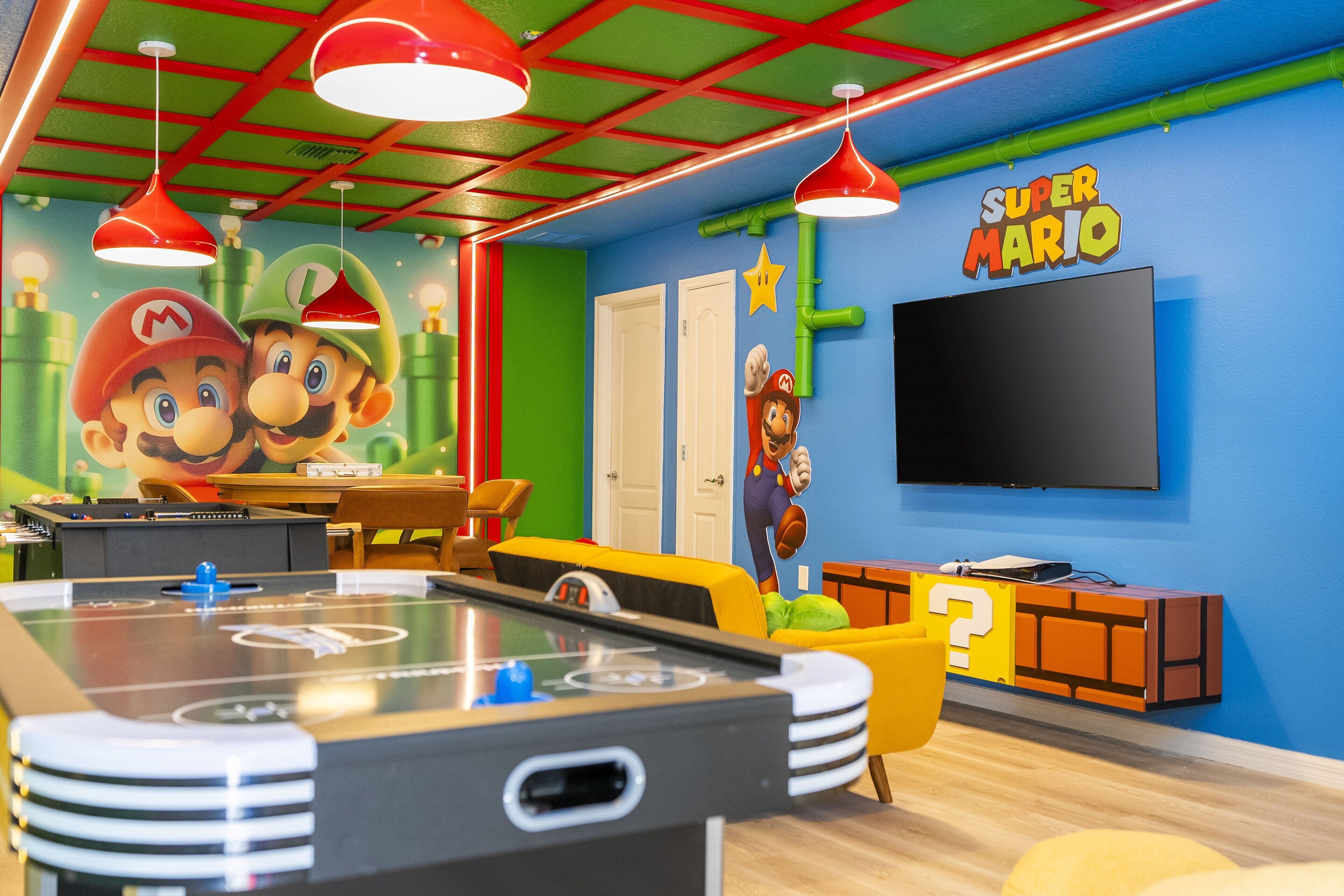 Een kamer met een pooltafel, een muurschildering met Mario-thema en een Super Mario televisiescherm.
