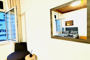 Ein Zimmer mit Bett, Stuhl, kleinem Tisch, Fenster und Spiegel, der den Raum widerspiegelt.