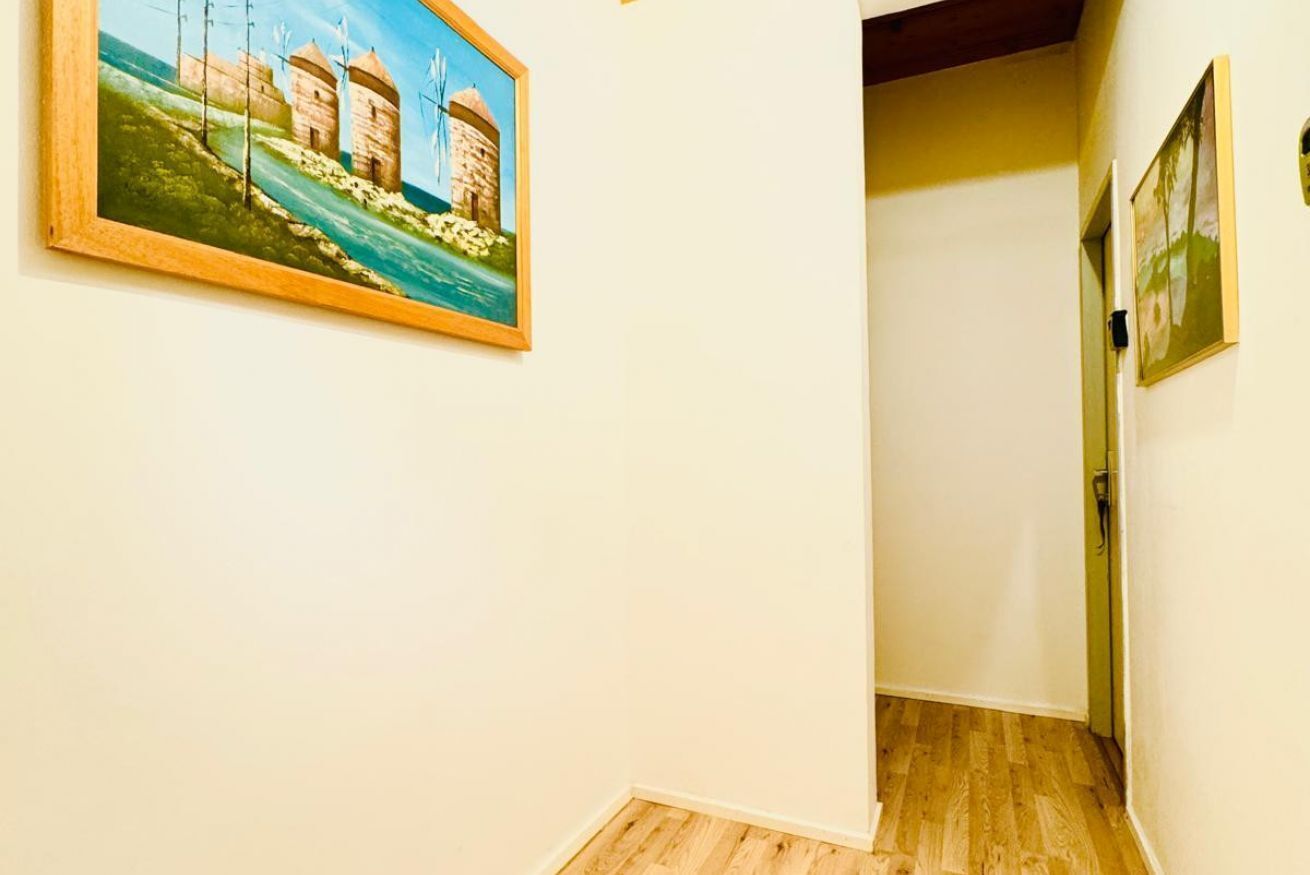 A hallway with a wooden floor, a painting of a coastal scene, and a door on the right.