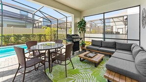 Ein moderner Außenbereich mit Pool, Grillplatz und einer Sitzecke mit Sofa und Sesseln.