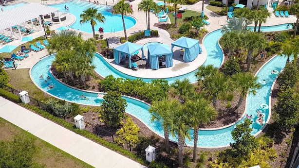 Luftaufnahme eines Resorts mit einem großen zentralen Pool, mehreren kleineren Pools und schattigen Liegebereichen mit Sonnenschirmen.