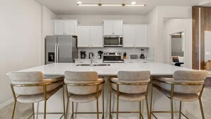 Una cocina moderna con armarios blancos, electrodomésticos de acero inoxidable y una isla central con taburetes de bar.