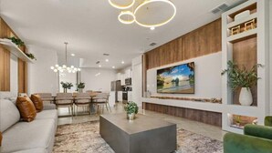 Una sala de estar moderna con un televisor grande, una zona de comedor y una cocina al fondo.