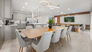 Eine moderne Küche mit einer zentralen Kochinsel, ein Essbereich mit einem Holztisch und Stühlen sowie eine Wohnbereich mit einer Couch und einem Fernseher.