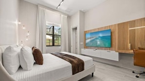 Ein modernes Schlafzimmer mit einem großen Bett, einem an der Wand montierten Fernseher und Blick ins Freie.