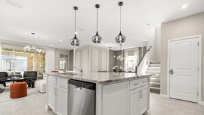 Una cocina moderna con armarios blancos, lavavajillas de acero inoxidable e iluminación colgante.