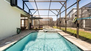 Una piscina con cerramiento de vidrio, mobiliario de patio y vistas del entorno.