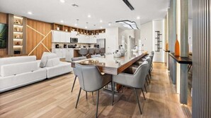A modern kitchen with white cabinets, a central island, and a dining area with a long table and chairs. - Last Minute Disney Getaway! Private Pool, Game Room & Themed Bedrooms. Book Now! #149063 (Orlando)
