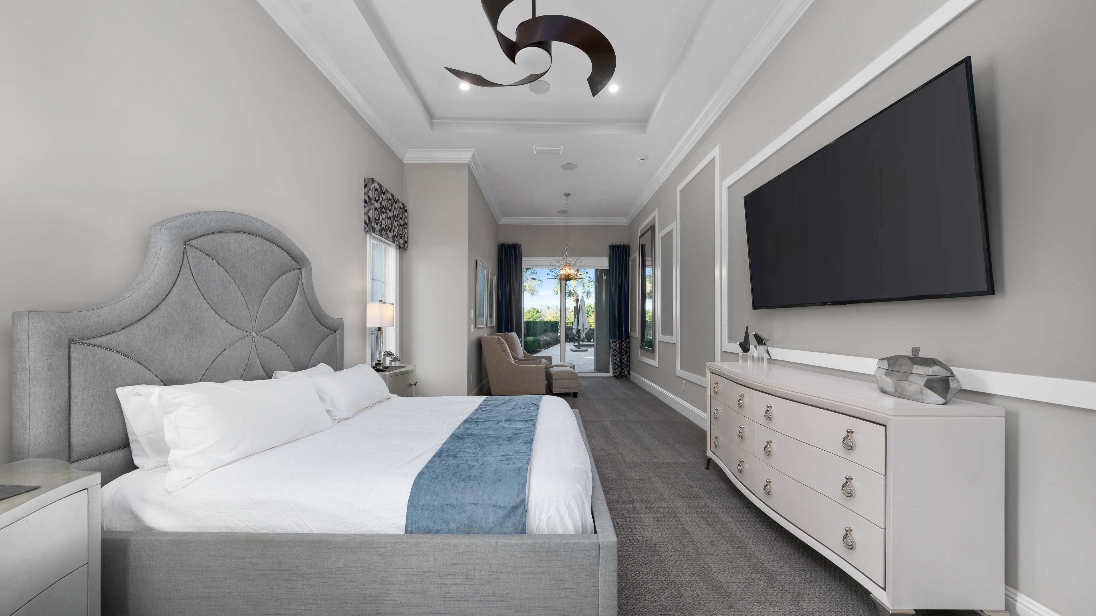 A modern bedroom with a large bed, a TV, a dresser, and a view to the outside.
