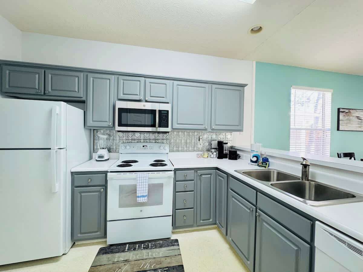 A kitchen with grey cabinets, a white refrigerator, a microwave, a stove, and a sink.