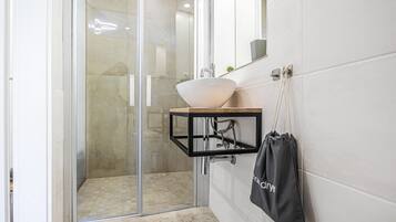 A modern bathroom with a glass shower enclosure, a white sink, and a towel rack.