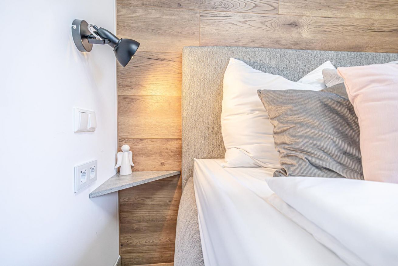 Une chambre à coucher moderne avec un lit, une table de chevet, une lampe fixée au mur et un mur d’accent en bois.