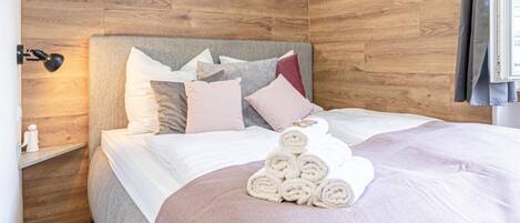 A neatly made bed with rolled towels, a bedside lamp, and a wooden headboard.