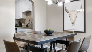 Un coin repas avec une table en bois, six chaises, un bol noir contenant une plante et, au mur, une œuvre d’art encadrée représentant la tête d’un taureau.