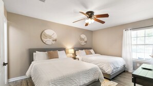 Une chambre avec deux lits, un ventilateur de plafond et une fenêtre avec des rideaux.
