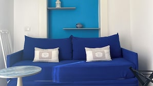 Un divano blu con due cuscini, un tavolino rotondo e una TV montata a parete.