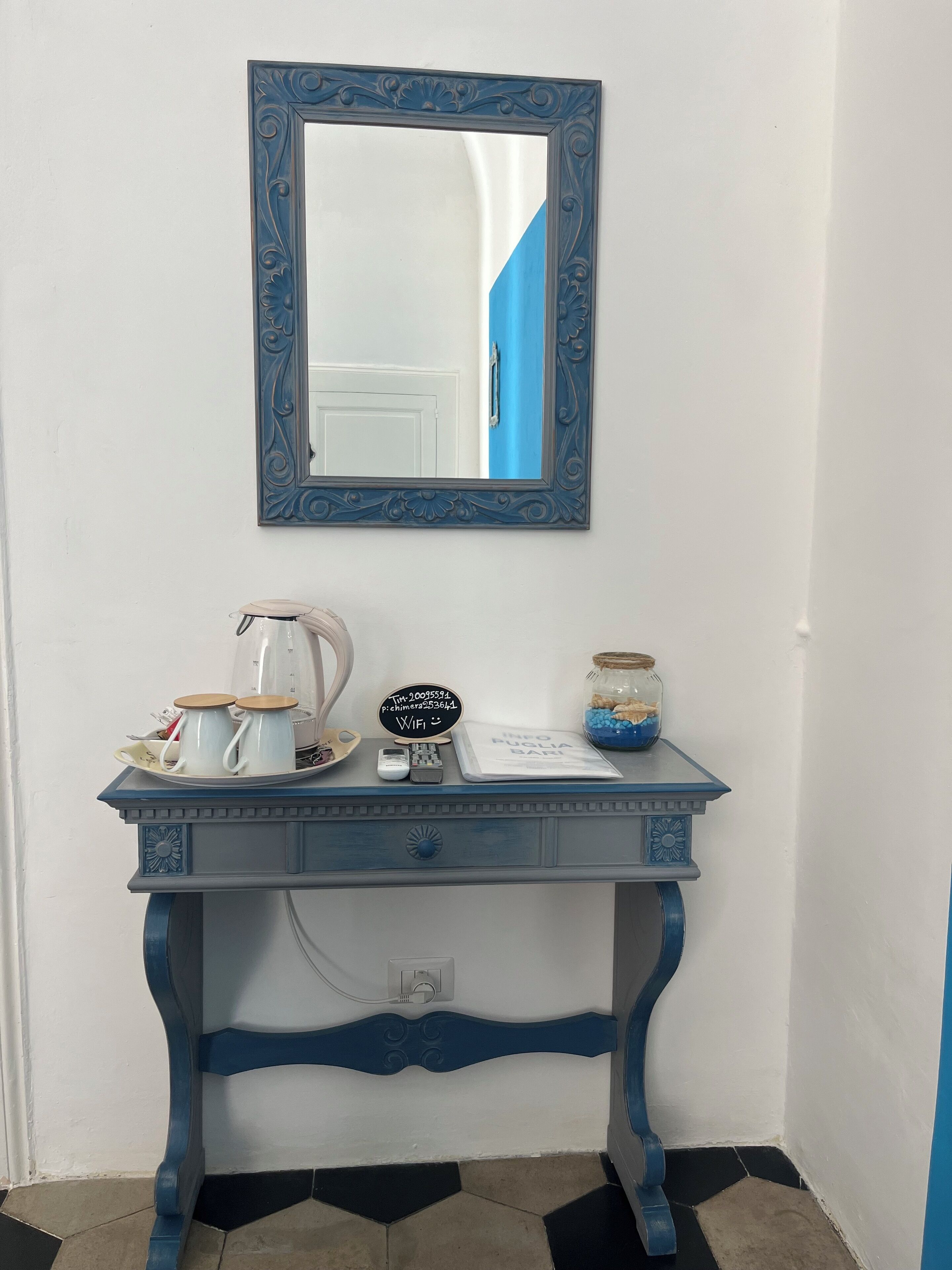 Una consola azul con un espejo decorativo encima, un cartel pequeño negro y un tarro de caramelos.